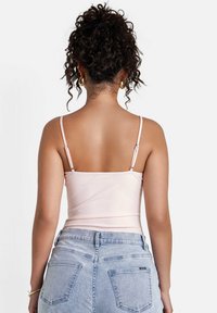 Ljusrosa åtsittande linne med tunna axelband, slät yta och sömlös design. Kombinerat med ljusblå högmidjade denimshorts.