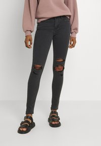 Jeans ajustados negros con detalles desgastados y rodillas rasgadas, hechos de denim. Combinados con sandalias negras de doble tira.