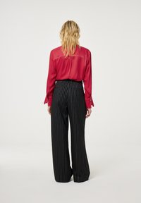Rode doorzichtige blouse met lange mouwen, bijpassende zwart gestreepte wijde broek. Kenmerken zijn gestructureerde schouders en verticale strepen.