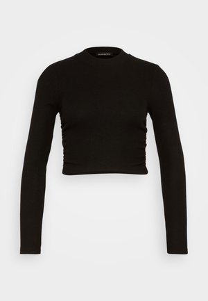 Un top cropped noir à manches longues en tissu côtelé, présentant un col haut et des détails froncés sur les côtés pour une silhouette ajustée.