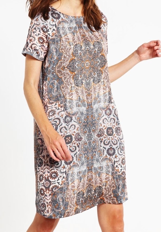 Femme portant une robe à manches courtes, longueur genou, avec des motifs floraux et géométriques symétriques complexes en marron, gris et blanc.