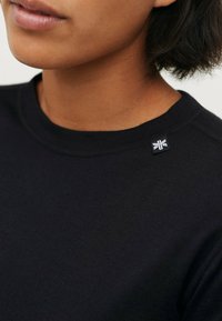 Zwarte katoenen crewneck T-shirt met een gestructureerde afwerking en een klein logopatch op de schouder. Minimalistisch ontwerp zonder patronen.