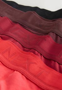 Four pairs of men's boxer briefs in gradient colors: black, dark red, burgundy, and bright red. Each has a textured waistband with "NEXT" logo.