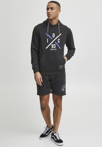 Black hoodie with white and blue graphic text, paired with black shorts featuring a small logo. Worn with black sneakers.