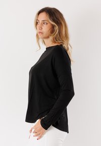 Maglietta nera a maniche lunghe con una vestibilità rilassata, scollatura rotonda e texture morbida. Senza motivi visibili, abbinata a pantaloni bianchi.