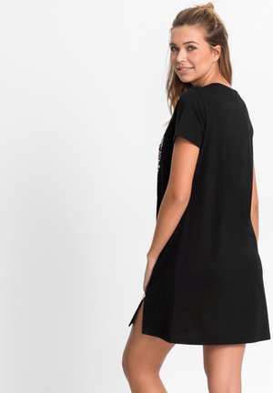 Robe noire à manches courtes en tissu doux, avec un col rond et des fentes latérales pour faciliter le mouvement, ornée de broderies florales sur le devant.