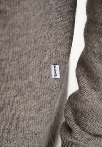 Gray knitted sweater featuring a soft texture, ribbed cuffs, and a rectangular brand label in white with black text.