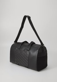 Sac de sport noir avec un corps en cuir lisse, un panneau d'accent texturé, des poignées solides, une sangle réglable et un panneau latéral en maille pour la respirabilité.