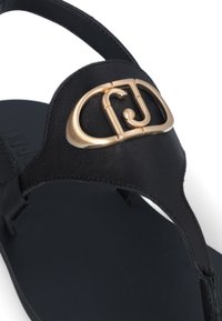 Sandale en cuir noir avec une accent en logo doré et une texture lisse. Design minimaliste avec une semelle plate.