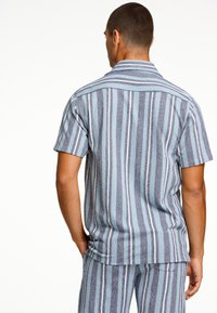 Camisetta a maniche corte con righe verticali blu e grigie, tessuto testurizzato, colletto aperto e vestibilità rilassata. Vista posteriore mostrata.