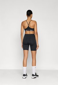 Μαύρο αθλητικό μπουστάκι με ρυθμιζόμενους ιμάντες, συνδυασμένο με μαύρο ποδηλατικό σορτς με ψηλή μέση. Λευκή λεπτομέρεια λογότυπου Nike στη ζώνη μέσης και στις κάλτσες.