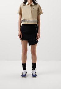 Krémové zkrácené polo tričko s límečkem a černými proužky na spodním lemu, spárované s pružnou černou mini sukni s t řepícími se okraji a bílými teniskami.