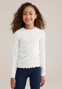 Chemise blanche à manches longues avec texture côtelée et ourlet festonné, assortie à un legging bleu marine ajusté. Le tissu semble doux et extensible.