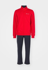 Chaqueta roja con cremallera y logo blanco, combinada con pantalones de chándal azul marino. Hecha de una tela suave, con un cuello alto y puños elásticos.