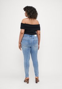 Juoda off-the-shoulder blusa su susiraukšlėjusiomis medžiagomis; šviesiai mėlyni ploni džinsai su klasikiniais užpakaliniais kišenėmis; rudos leopardo rašto aukštakulniai.