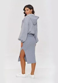 Szary komplet dresowy składający się z bluzy z kapturem i dopasowanej spódnicy, wykonany z miękkiego materiału; spódnica ma boczny rozcięcie, a całość zestawiona z białymi sneakersami.