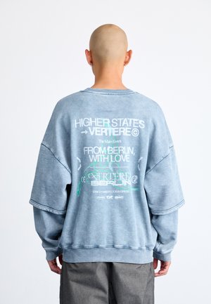 Felpa oversize azzurro chiaro con grafiche testuali bianche e verdi sul retro. Realizzata in materiale morbido con collo e polsini a costine.