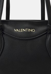 Svart läderhandväska med en strukturerad yta, med en guldig "VALENTINO"-logotyp och två robusta handtag.