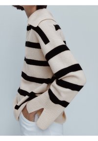 Beige trui met zwarte strepen, voorzien van een kraag en brede geribbelde mouwen. Gemaakt van een zacht gebreide stof.