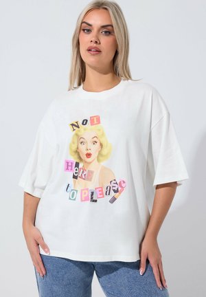 Donna che indossa una maglietta bianca oversize con un'illustrazione in stile retrò di una donna bionda e un collage di testo colorato con la scritta "Non sono qui per piacere" e un'icona di rossetto.