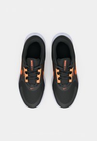 Černé sportovní boty s oranžovými akcenty, texturovaný síťovaný svršek, ploché šněrování a bílá gumová podrážka, s logem na každé straně.
