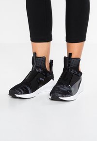 Svarta träningsskor med en elegant design, övre del i mesh, vadderad krage och vita sulor. Har logotypdetaljer och ett strukturerat mönster.