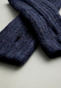 Marineblå strikket uldscarf med struktureret overflade, der har lodrette ribbede mønstre og et blødt, tykt udseende, viklet i en krydset position.