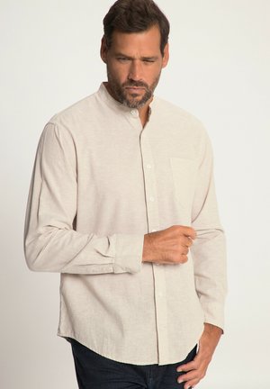 Camisa de botones color beige claro con cuello mandarín, mangas largas, bolsillo en el pecho y un tejido suave y texturizado. El dobladillo es curvado.