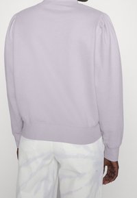 Ljuslila sweatshirt med puffärmar, ribbad mudd och nederkant, tillverkad av mjukt tyg, ihopparad med vita tie-dye-byxor.