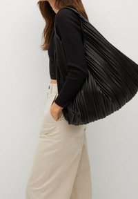 Black pleated hobo bag made of synthetic material, featuring a soft texture and spacious shape, worn over a shoulder with casual clothing.
