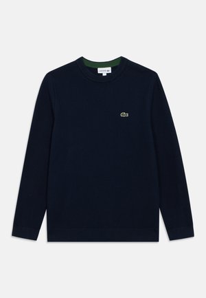 Tamsiai mėlynas megztinis, pagamintas iš mezgamo audinio, su apvalia apykakle, ilgomis rankovėmis ir mažu žaliu "Lacoste" logotipu ant krūtinės.