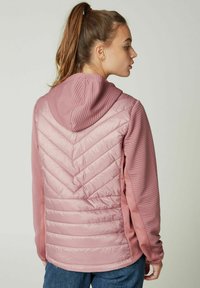 Lyserød hættejakke med et chevron-quiltet design på ryggen, ribbet tekstur på ærmerne og en glat finish, velegnet til afslappet brug.