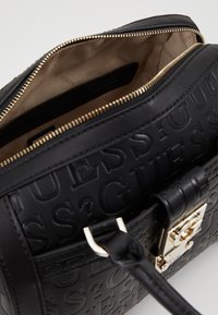 Zwarte reliëf neplederen handtas met gouden hardware, voorzien van een ritssluiting en een beige interieurafwerking met merkdetails.