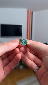 Srebrn prstan s kvadratnim turkiznim vložkom, ki ima odtisnjen srčni motiv. Gladek površinski sijaj, poliran zaključek, minimalističen slog.