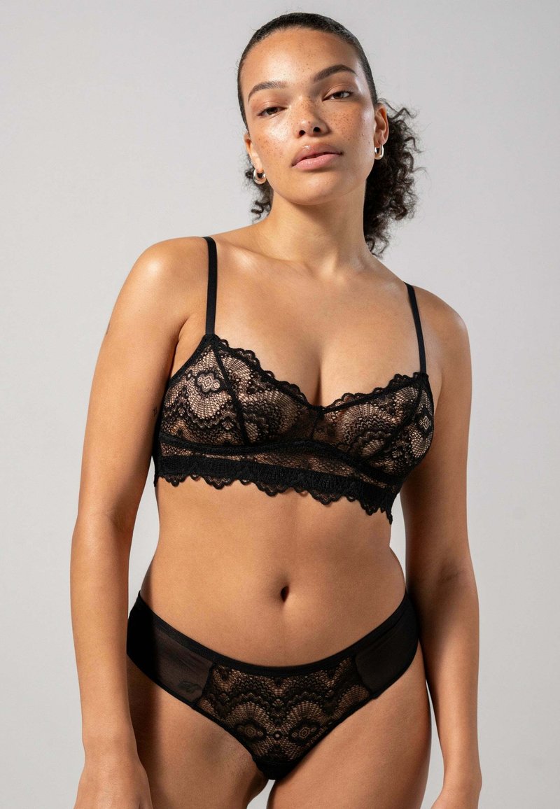 Svart spets-bh och matchande trosor, med scallopade kanter och genomskinliga detaljer. Mjuk, delikat textur med intrikata mönster.