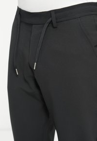 Pantaloni negri dintr-un material elastic și neted; au talie cu șnur, buzunare frontale și un design ajustat.