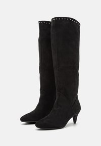 Bottes hautes en daim noir jusqu'au genou avec un bout effilé, un petit talon kitten bas, et des clous décoratifs le long du bord supérieur. Texture lisse et design ajusté.