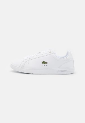 Zapatilla blanca de caña baja con cierre de cordones, logo de cocodrilo verde en el lateral y marca Lacoste en la suela sobre un fondo liso.