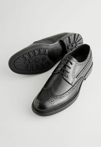 Chaussures en cuir noir avec détails en brogue, semelle en caoutchouc et design à lacets. Présentent une texture lisse et des perforations décoratives.