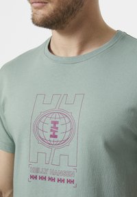 Lichtgroen katoenen t-shirt met een cirkelvormige wereldbolafbeelding en de tekst "Helly Hansen" in paars. Ronde halslijn en korte mouwen.