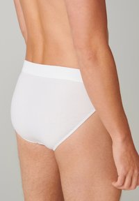 Weiße Baumwollslips mit einem weichen, elastischen Bund, die eine glatte Textur und eine enge Passform aufweisen, gezeigt aus der Rückansicht und im Profil.