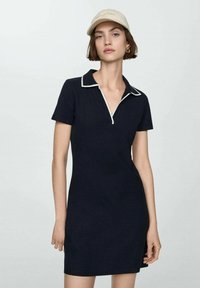 Marineblå polo kjole med korte ærmer, krave og kontrastfarvet hvid kant. Stoffet ser blødt og tætsiddende ud, med sidelommer.