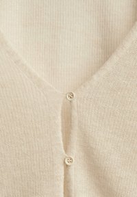 Tissu en maille de couleur crème douce avec deux petits boutons assortis fermant une ouverture en V.