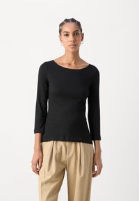 Top negro de manga larga con cuello redondo, diseño ajustado y textura suave, combinado con pantalones claros con pliegues.