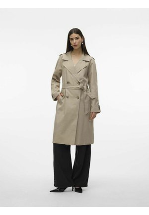 Beige trench coat s dvoubarevným designem, širokým límcem a páskem v pase. V kombinaci s černými širokými kalhotami a špičatými podpatky.
