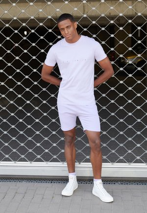 Light purple two-piece outfit consisting of a short-sleeve t-shirt and shorts. The shirt features a minimalist text design. White high-top sneakers.