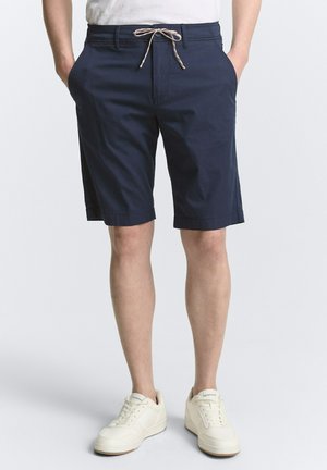 Marineblauwe shorts met een trekkoord in de taille, zijzakken en omgeslagen zoom. Draag ze met witte sneakers, met een strak ontwerp en textuur.
