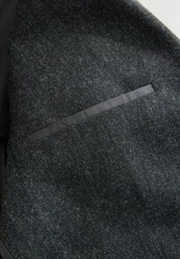 Dunkelgrauer Wollmix-Stoff mit einer strukturierten Oberfläche, der ein schlankes, schwarzes Satin-Taschendetail aufweist. Das Material wirkt weich und edel.