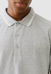 Grijze polo gemaakt van een katoenmix, met een geribbelde kraag met witte strepen en een tonale geborduurde logo op de borst.