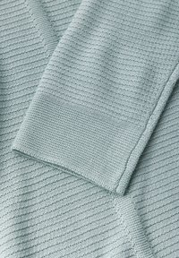 Pull en tricot bleu clair avec un design texturé, présentant de fines rayures et un poignet côtelé. Matière douce avec une coupe légèrement ample.